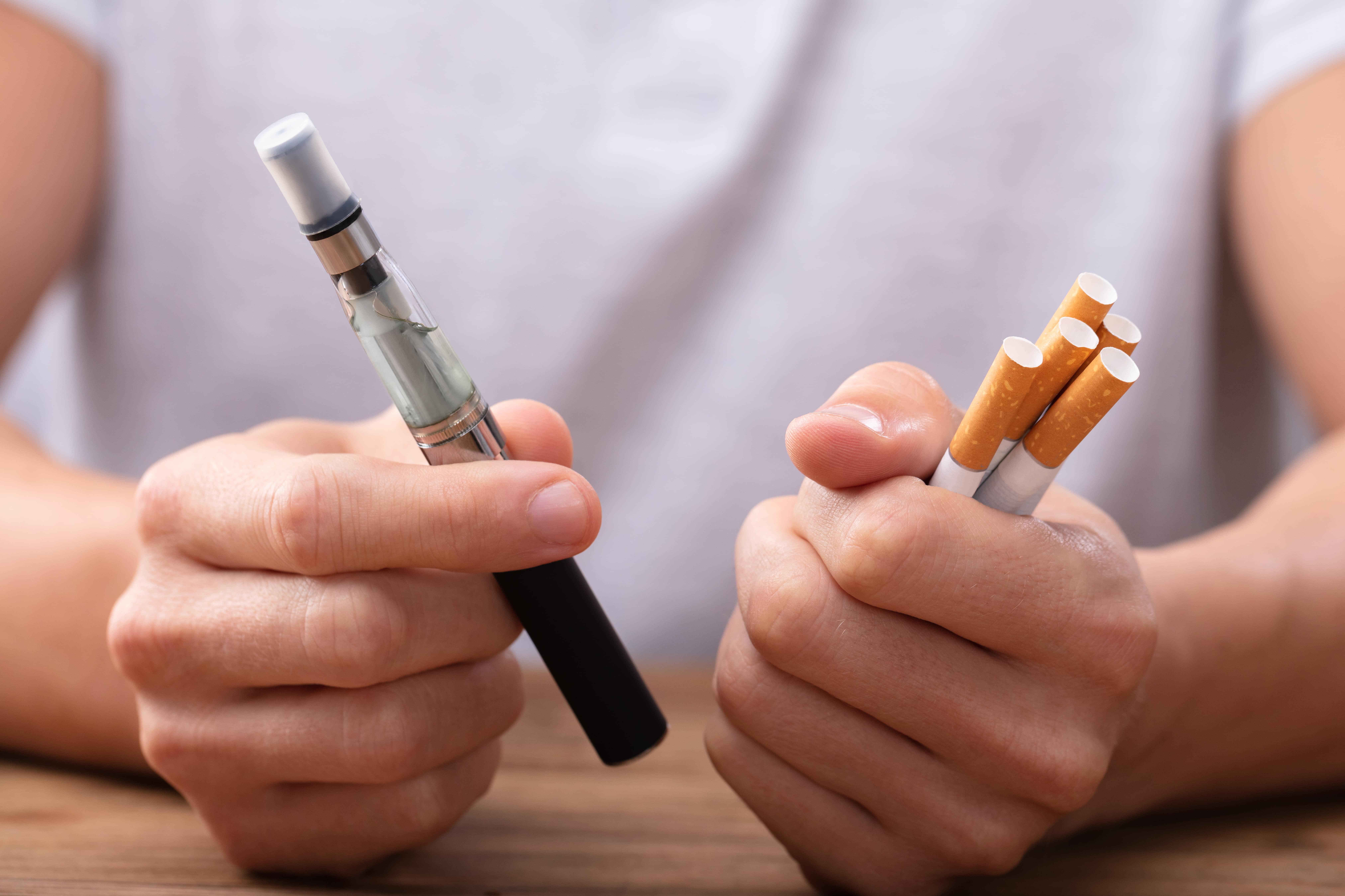 Twee handen met vape en sigaretten